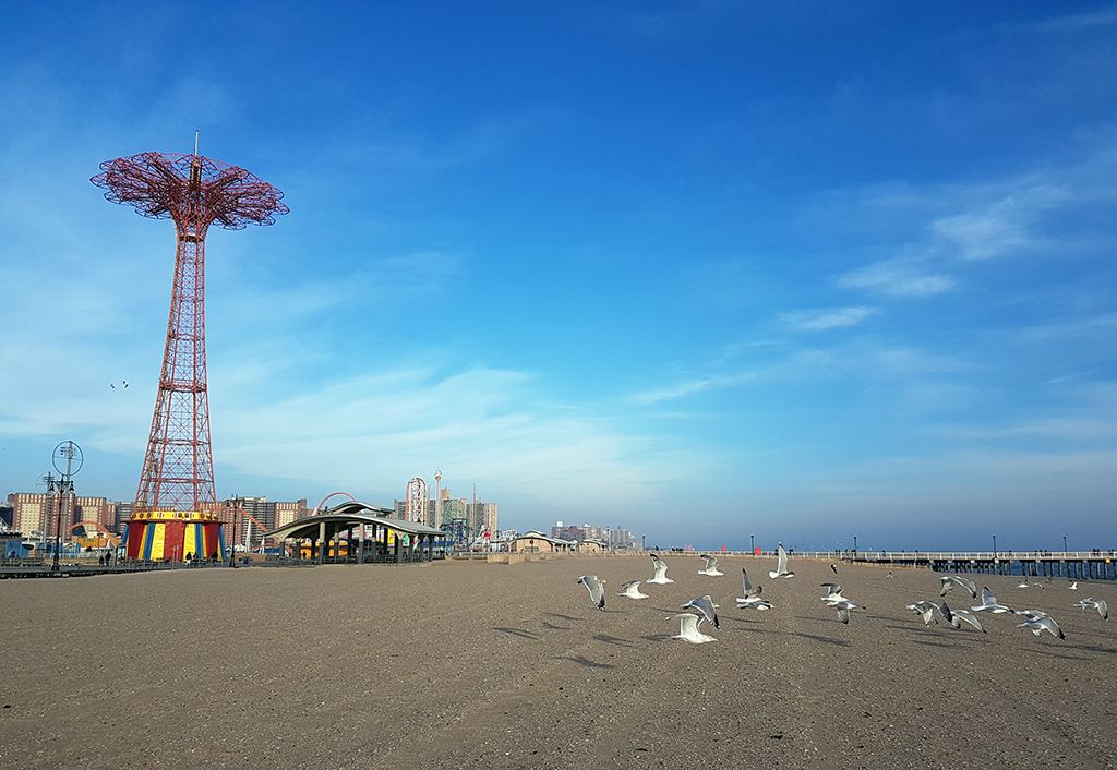 Vista panorámica de la playa y el paseo martítimo de Coney Island, a la izquierda se ve el antiguo juego mecánico PARACHUTE. Guía de las Playas de Nueva York. Foto de Andrea Hoare Madrid