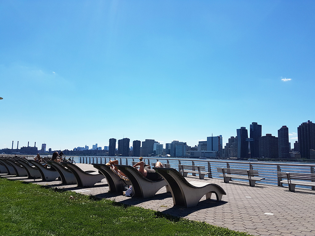 Personas descansando en las bancas del Gantry Plaza State Park en Queens - Vistas de Midtown Manhattan al otro lado del East River - Foto de Andrea Hoare Madrid