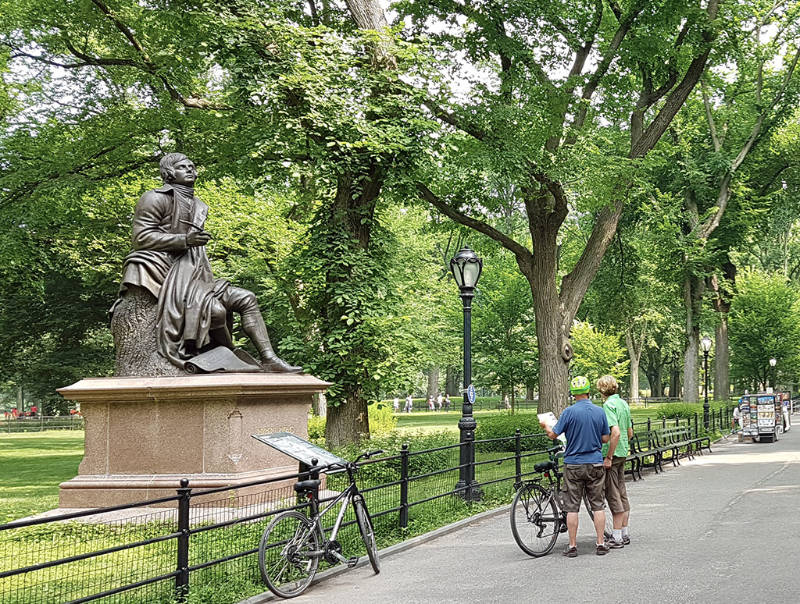 Turistas realizando un tour en bicicleta por Parque Central, están detenidos mirando una de las esculturas del Paseo de los Literatos - Foto de AHM