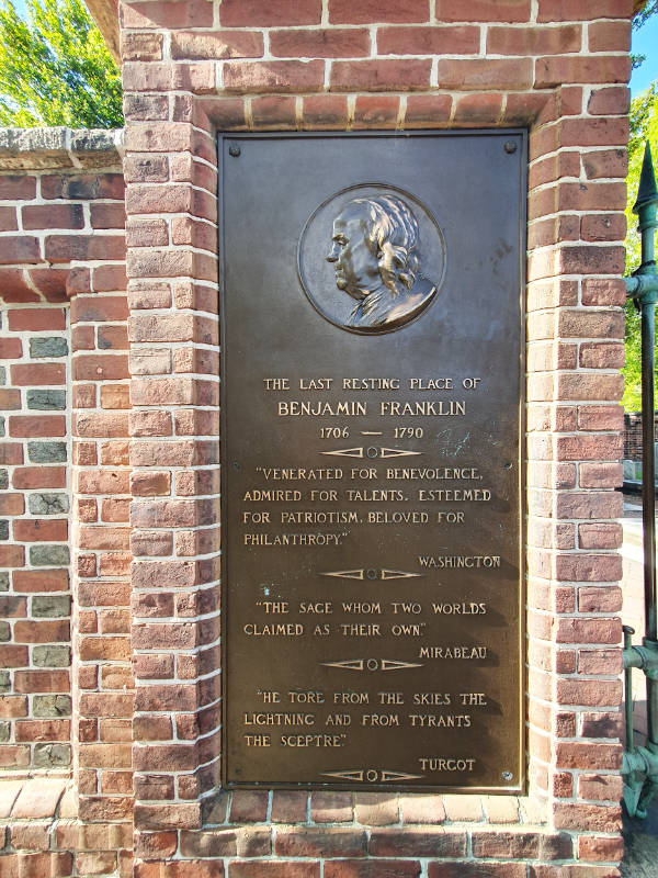 Placa de bronce conmemorativa a Benjamin Franklin a la entrada del Cementerio Christ Church en la calle Arch en Filadelfia. Se ve una efigie de Franklin y se leen varios elogios entre ellos el de Washington: "Venerado por su benevolencia, admirado por sus talentos, estimado por su patriotismo y amado por su filantropía". Foto de Andrea Hoare Madrid