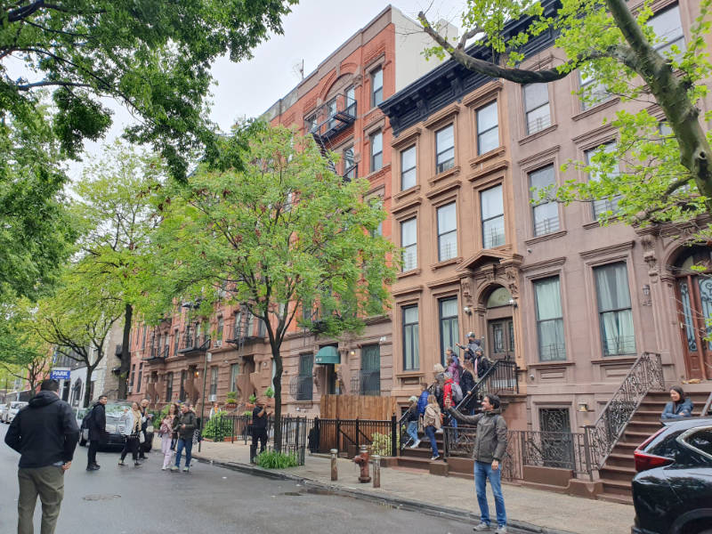 Típica calle de Brownstones de Harlem, que son viviendas pareadas de máximo 4 pisos y escaleras en la entrada. Se ven turistas tomándose fotos frente a las casas. Foto de Andrea Hoare Madrid