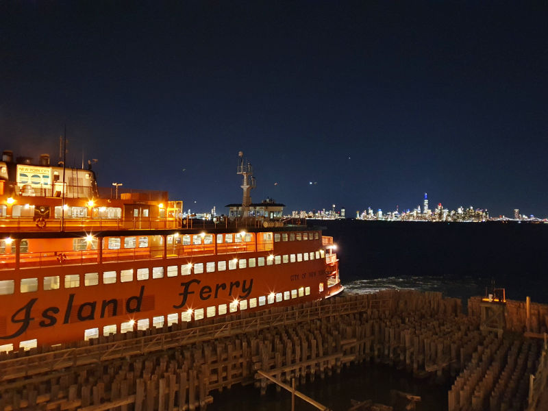 Ferry Staten Island en el Terminal St. George. Es de noche, todas las luces del ferry están encendidas, al fondo se ve el sklyline de Manhattan iluminado. Foto de Andrea Hoare Madrid